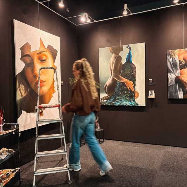 Vandaag is het opbouwen… en geloof me, het is alles behalve glamorous 😅

Ik sta hier nu in het Autotron voor de opbouw van de Art of Living Event. En als je denkt dat het hier al helemaal strak en mooi is… nee hoor.

Overal spullen.
Doeken tegen de muur.
Verpakkingsmateriaal op de grond.
Mensen die heen en weer lopen.

En ik ondertussen:

“Moet ik deze hier hangen?”
“Of toch daar?”
“Is dit niet te druk?”
“Of juist te leeg?”

Het gaat echt alle kanten op in mijn hoofd.

Dit is dus dat stukje wat je straks niet meer ziet.
Als alles hangt. Als het klopt. Als het “af” voelt.

Maar nu… is het gewoon bouwen. Schuiven. Twijfelen. Nog een keer kijken.

En ergens hoort dat er ook bij.

Want dit is ook een soort afsluiting van de afgelopen periode. Alle uren in mijn atelier. De stress. De druk. Het willen dat alles goed genoeg is.

En nu sta ik hier.

Klaar om het straks te laten zien.

Dus ja… tussen de chaos en de twijfel door…
heb ik er vooral heel veel zin in 💛

—
Wie ben ik?
Emily van de Wiel

Ik ben kunstenares, gespecialiseerd in hyperrealistische schilderijen die vrouwelijke kracht en kwetsbaarheid vangen. Mijn werk draait om detail, licht en intimiteit. Vaak persoonlijk, soms rauw, maar altijd echt. Ik maak zowel vrij werk als schilderijen in opdracht, ieder doek met liefde en precisie geschilderd.

Laten we connecten!